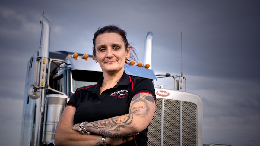 A woman with her arms folded stands in front of a truck. 