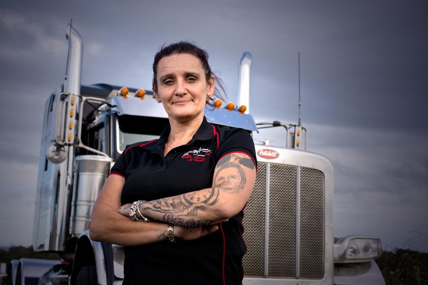 A woman with her arms folded stands in front of a truck. 