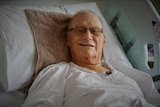 A man lies in a hospital bed and smiles at the camera