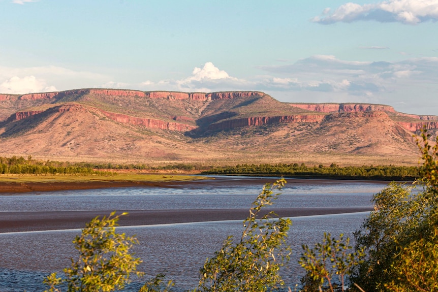 a river with multi-tiered orange mesa hills in the distance