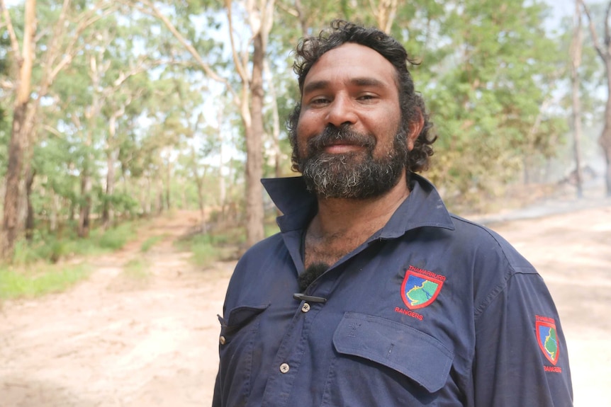 Uriah Crocombe is standing in front of bushland that has recently been set on fire.