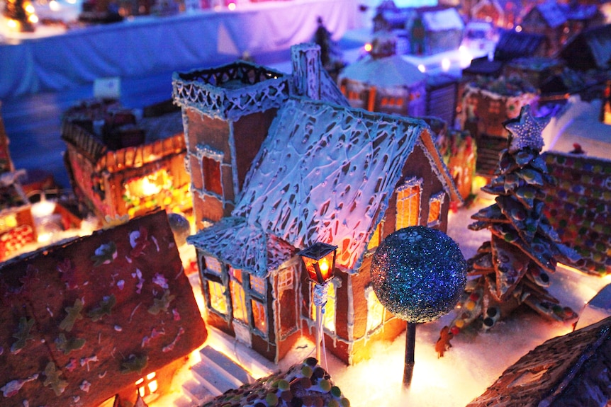A model made from gingerbread of a pitched-roof home with a tree in its yard and a tower on its right side.