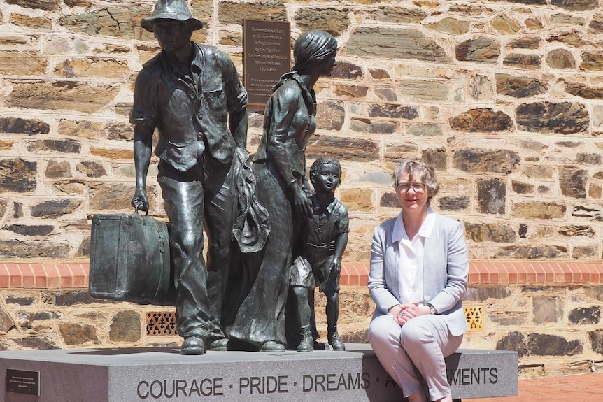 A woman sits by a monument of migrants in Adelaide