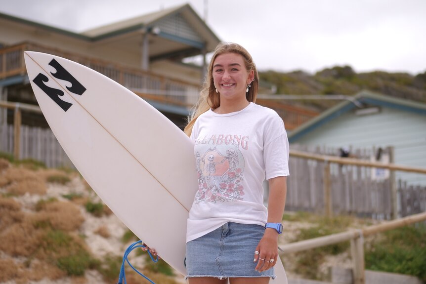 A teenage girl holding a surfboard in front of a surf club 