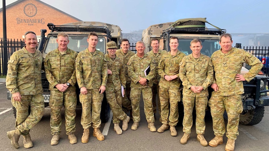 Male army officers stand in front of their vehicles at the Bundaberg Rum Distillery