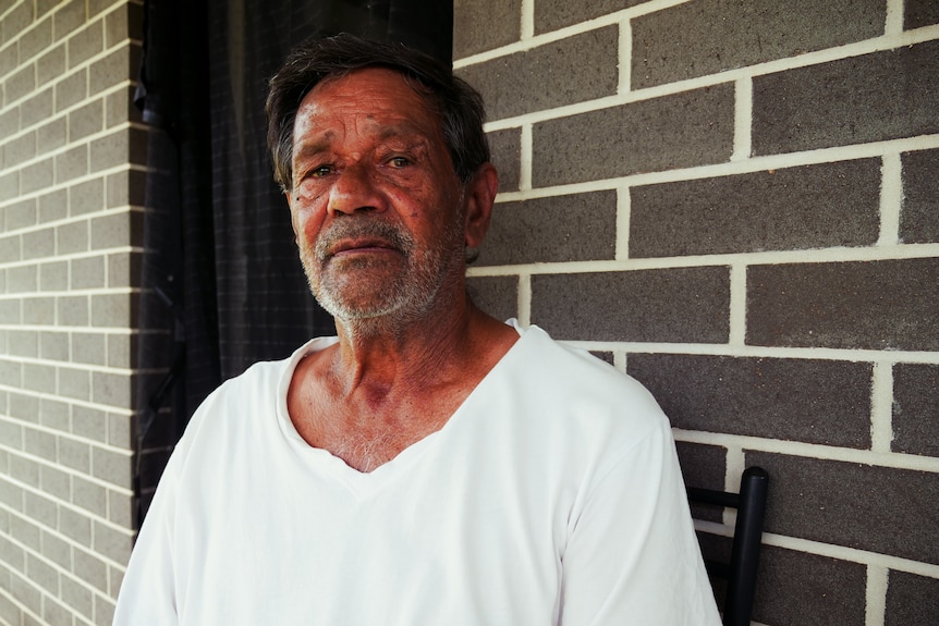 Man in white shirt sits in front of grey brick wall.