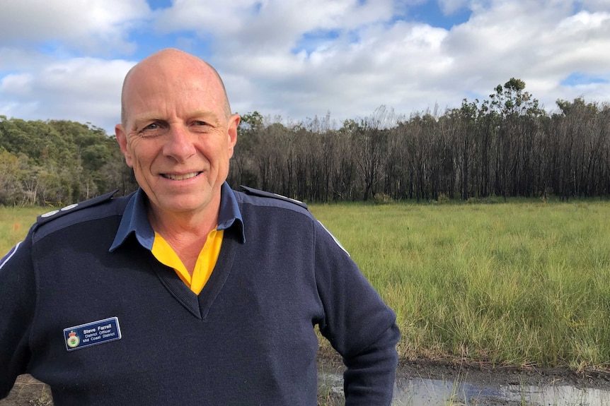 A man in RFS uniform stands in front of burnt trees.