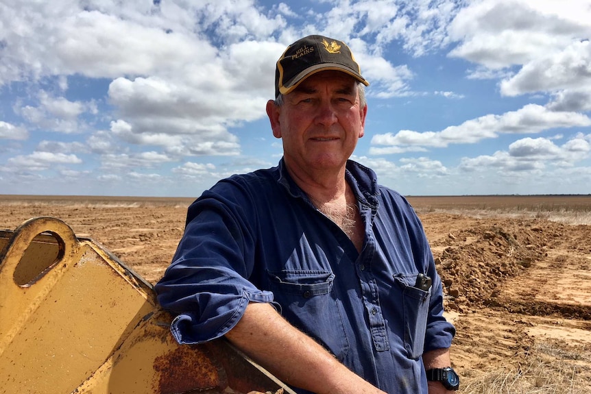 A man standing in a paddock with some of his machinery