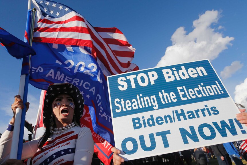 Supporters of President Donald Trump hold US flags and a sign saying 'Stop Biden stealing the election'.