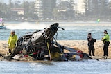 The wreckage of a helicopter on a sand bank with emergency services standing nearby