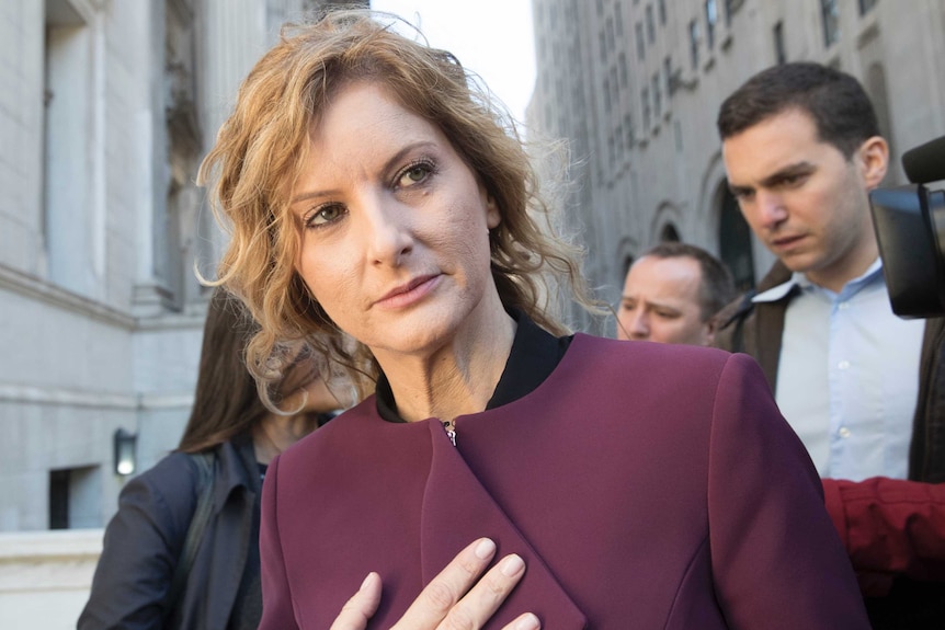 A close up image of a woman whose face is lit by flash bulbs leaves a neoclassical building wearing a burgundy zip jacket.