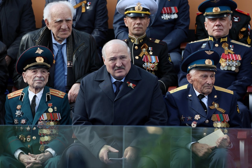 Alexander Lukashenko sitting between rows of people in decorated soldier uniforms. 