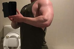 A selfie taken in a bathroom shows a man, with his head out of frame, flexing his muscles.