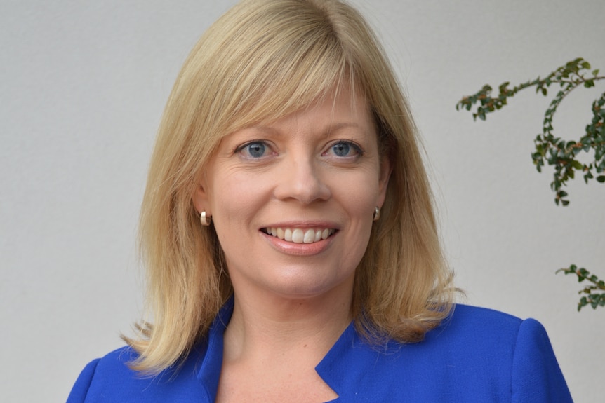 A woman with blond hair and a blue suit smiles.