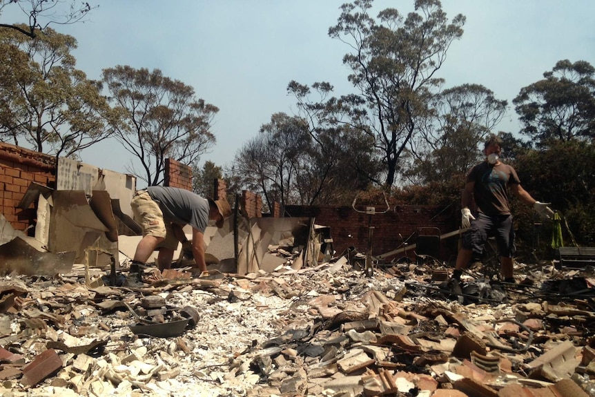 Two men sort through rubble at a fire damaged house