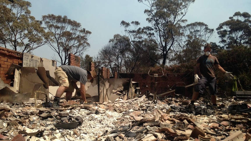 Two men sort through rubble at a fire damaged house