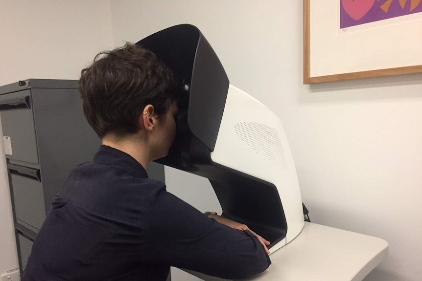 A woman sits with her head resting in a white metal box.