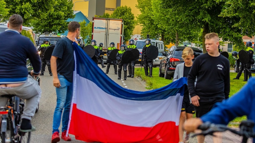 Protesters hold a Dutch flag as police look on.