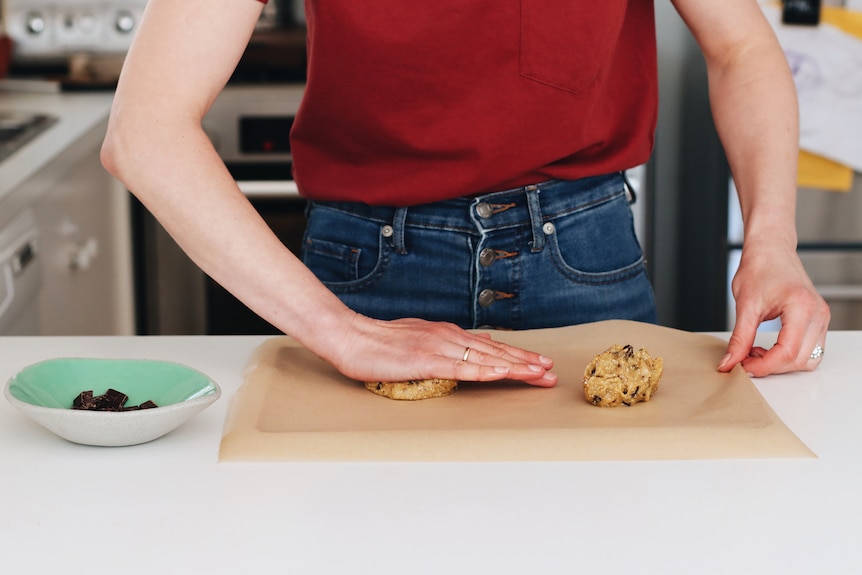 A person presses cookie dough down on a baking tray to make sure it bakes evenly, making giant choc chunk cookies.
