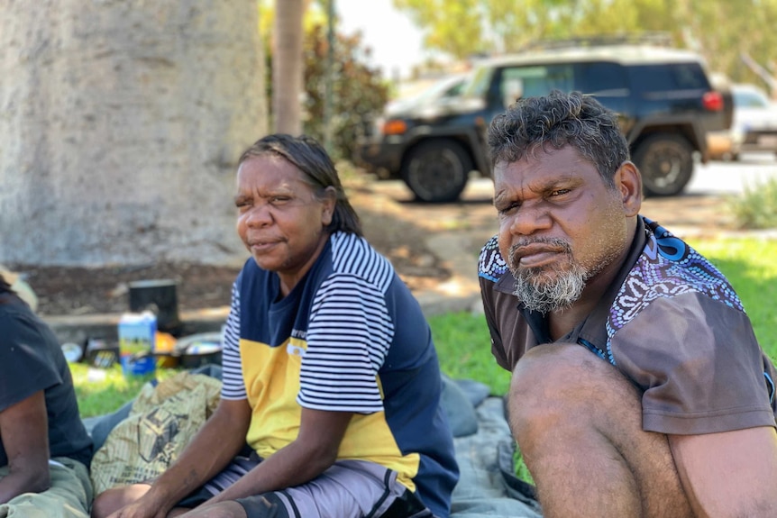 An Aboriginal woman and man sit together under the shade of a tree in Broome.