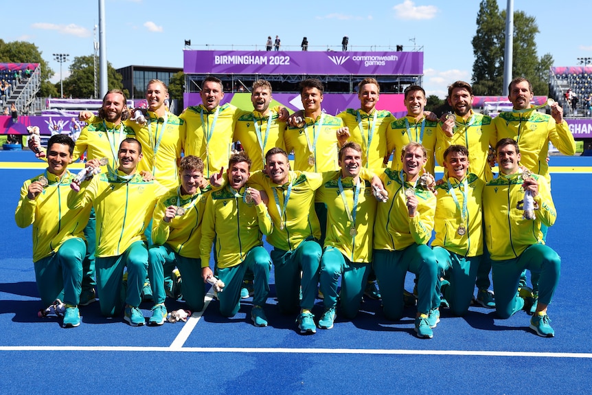 A men's hockey team wearing yellow and green pose with medals after a final game