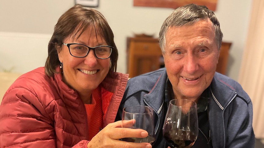 A daughter and father hold up glasses of red wine.
