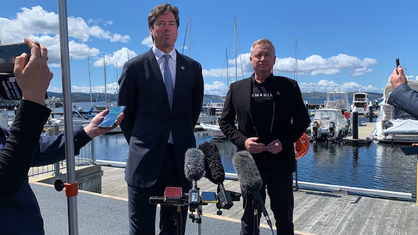 Two men in front of microphones on Hobart's waterfront in front of docked boats.