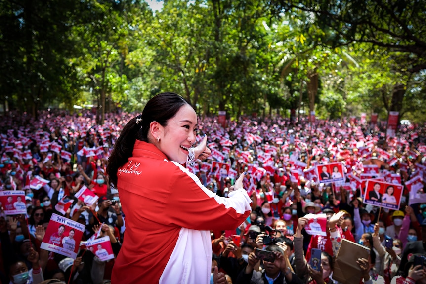 A Thai woman in a red jacket stands in front of a huge crowd