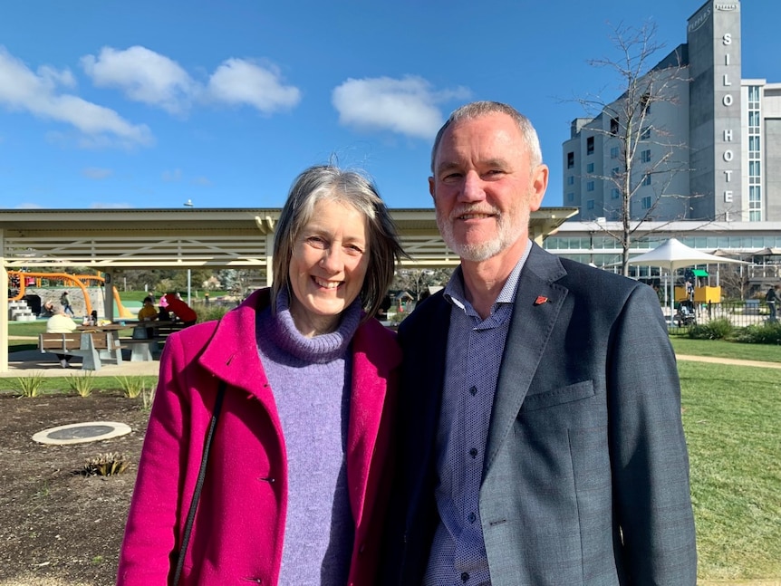 A man and a woman stand in the sun smiling 