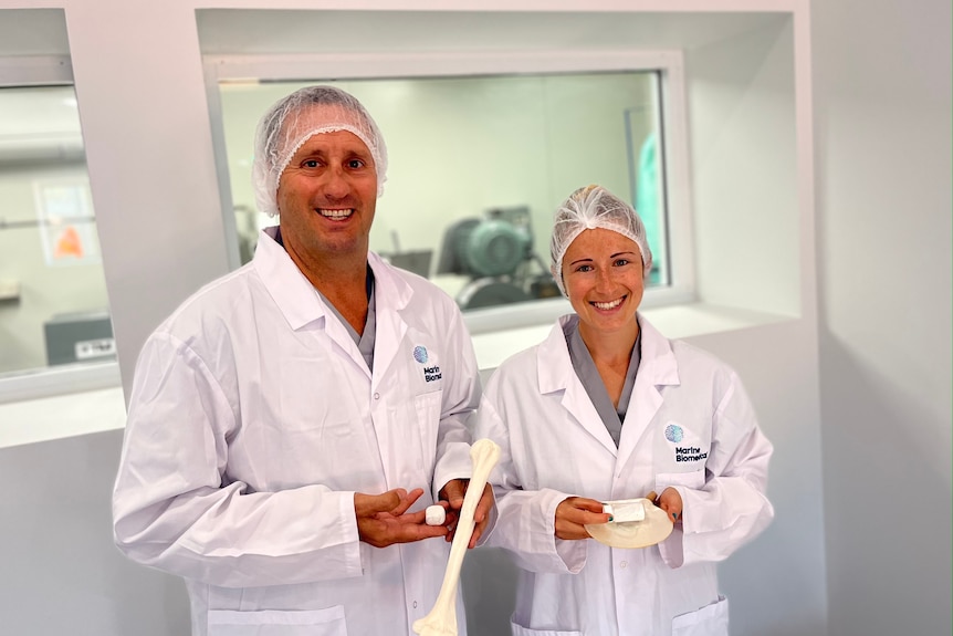Two people, wearing hair nets and white coats, stand in a laboratory.