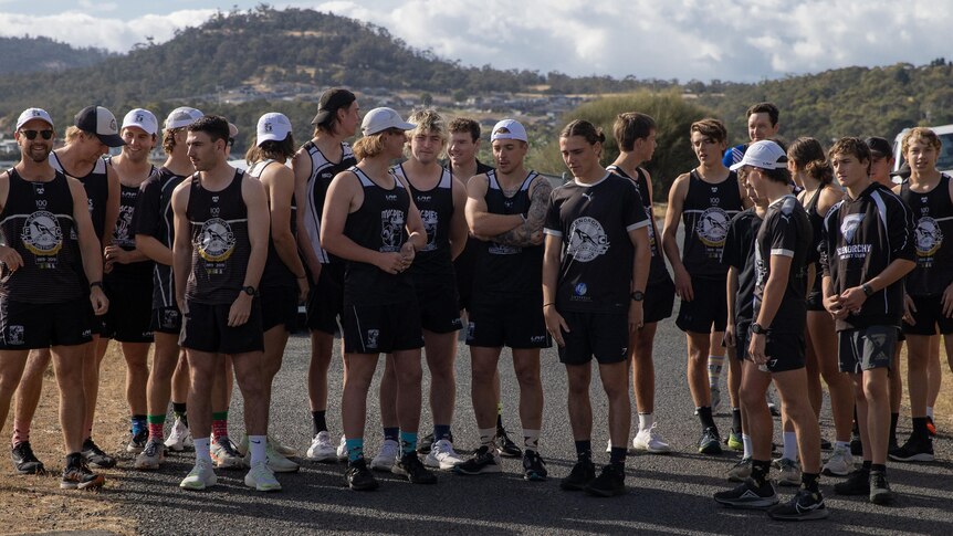 A group photo of nearly two dozen young men in running gear standing on a road.