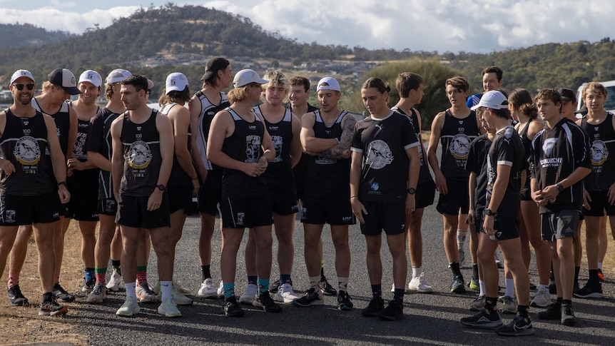 A group photo of nearly two dozen young men in running gear standing on a road.