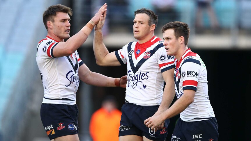 Two male NRL players give each other a high five as their teammate walks alongside them.