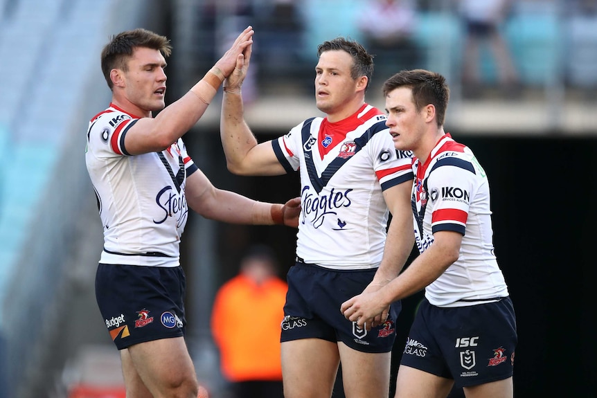 Two male NRL players give each other a high five as their teammate walks alongside them.