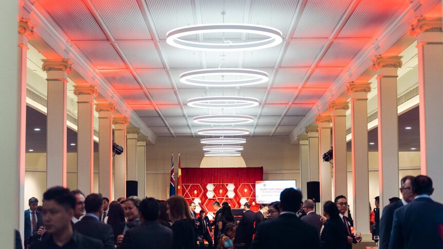 A crowd inside the Government House ballroom lit up with red lights.