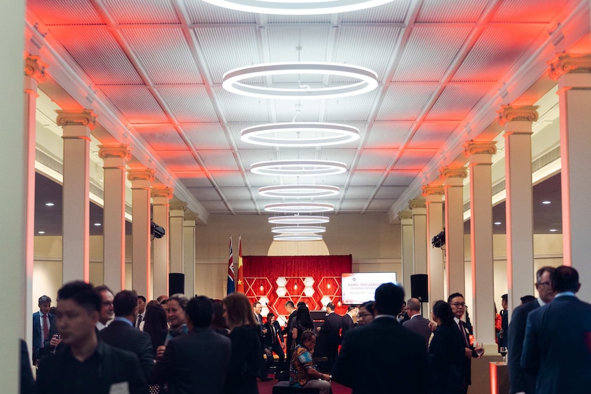 A crowd inside the Government House ballroom lit up with red lights.