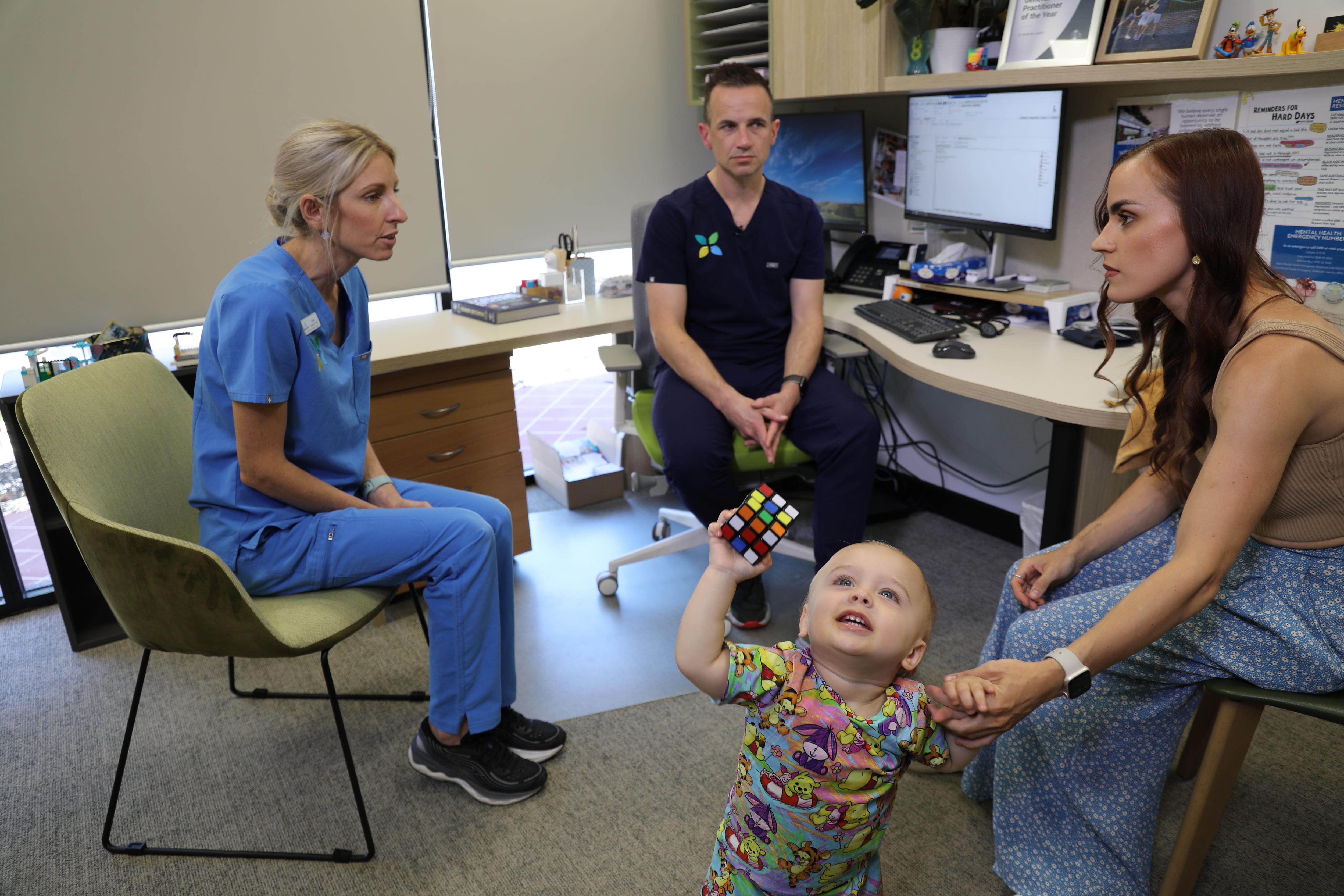 Lianne sitting in treatment room talking to doctor and nurse, holding onto 14-month old son