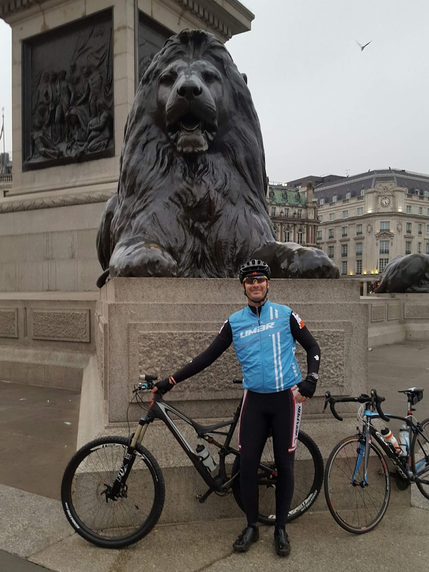 Man with bicycle stands in front of statue of lion