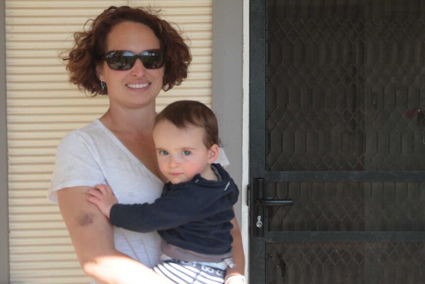 Broken Hill Stay at home mum, Emma Ward, holds her young son in front of their house in Broken Hill.