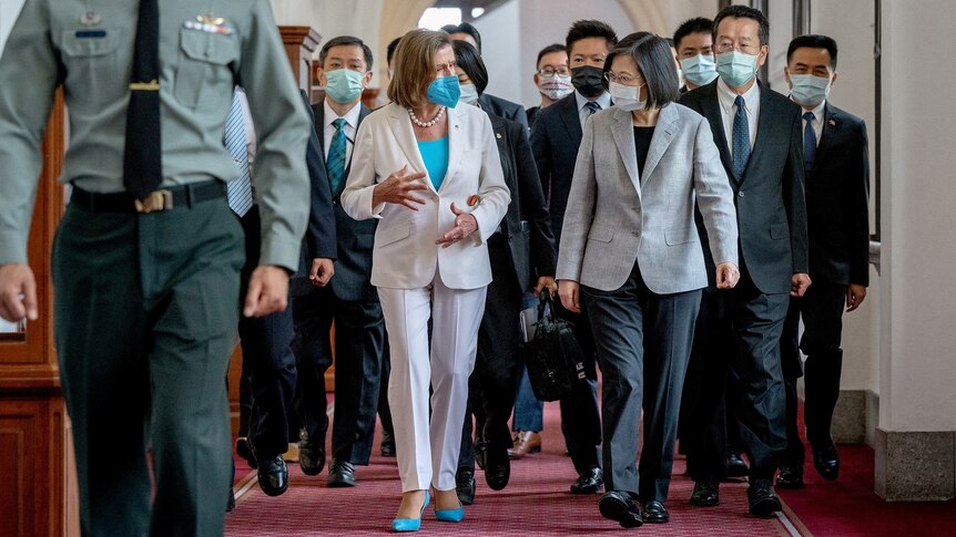 A line of people in business attire and masks walk down a corridor