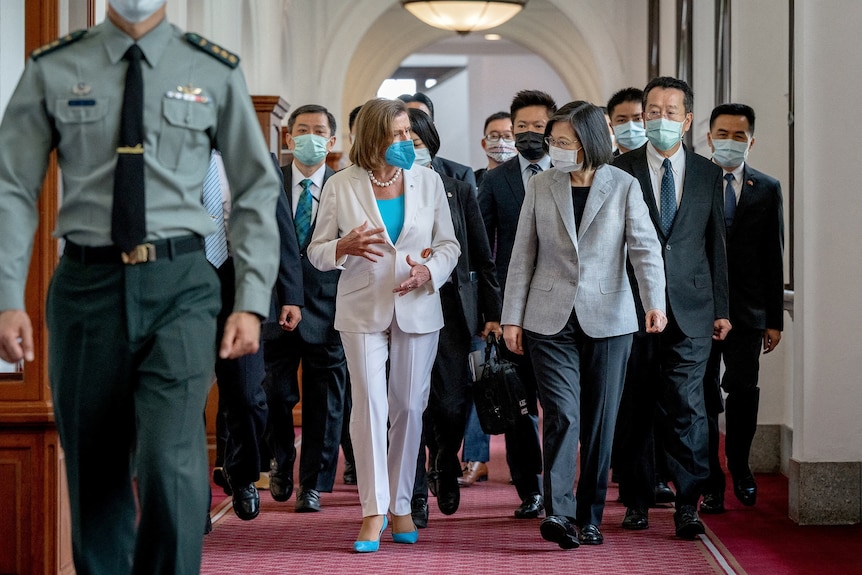 A line of people in business attire and masks walk down a corridor