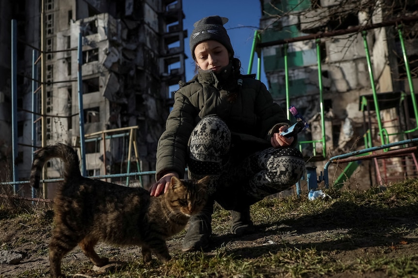 Veronika Krasevych feeds a feral cat near her destroyed building in Borodianka
