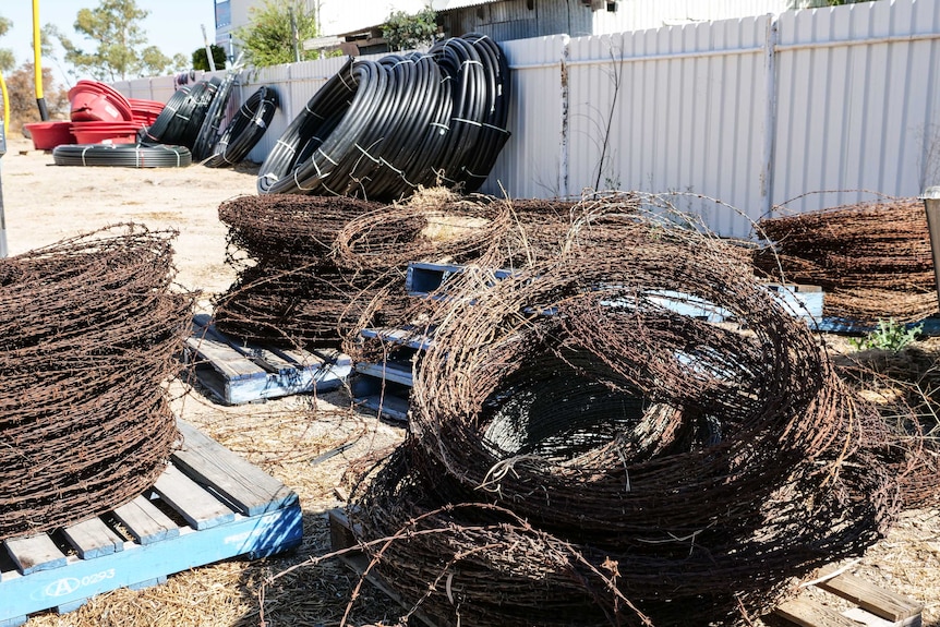 Piles of barbed wire, in circles, are placed on pallets outside.