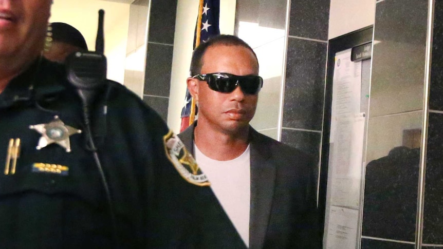 Golfer Tiger Woods makes his way into the North County Courthouse. He is wearing sunglasses and is surrounded by police.