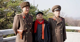 Two soldiers stand with a man dressed in a black jacket.