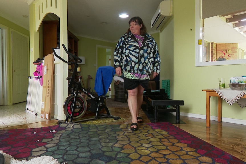 Anita walks across sodden carpet looking at the water damage to her home