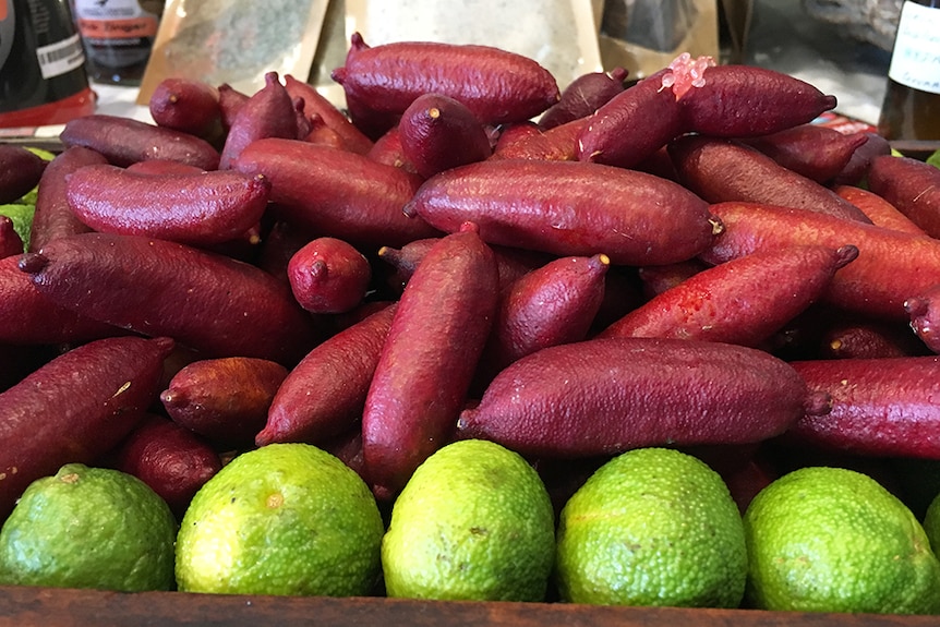 A pile of red finger limes and green kaffir limes in a crate.