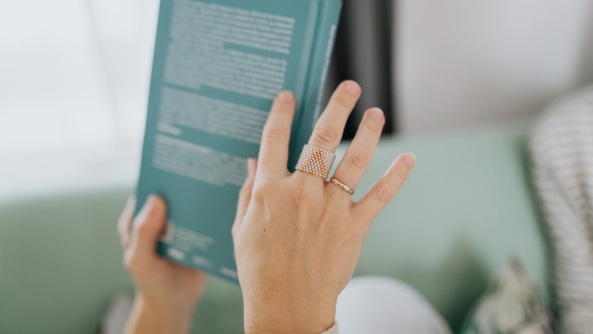 a hand holding a book from the back and pointing to cover