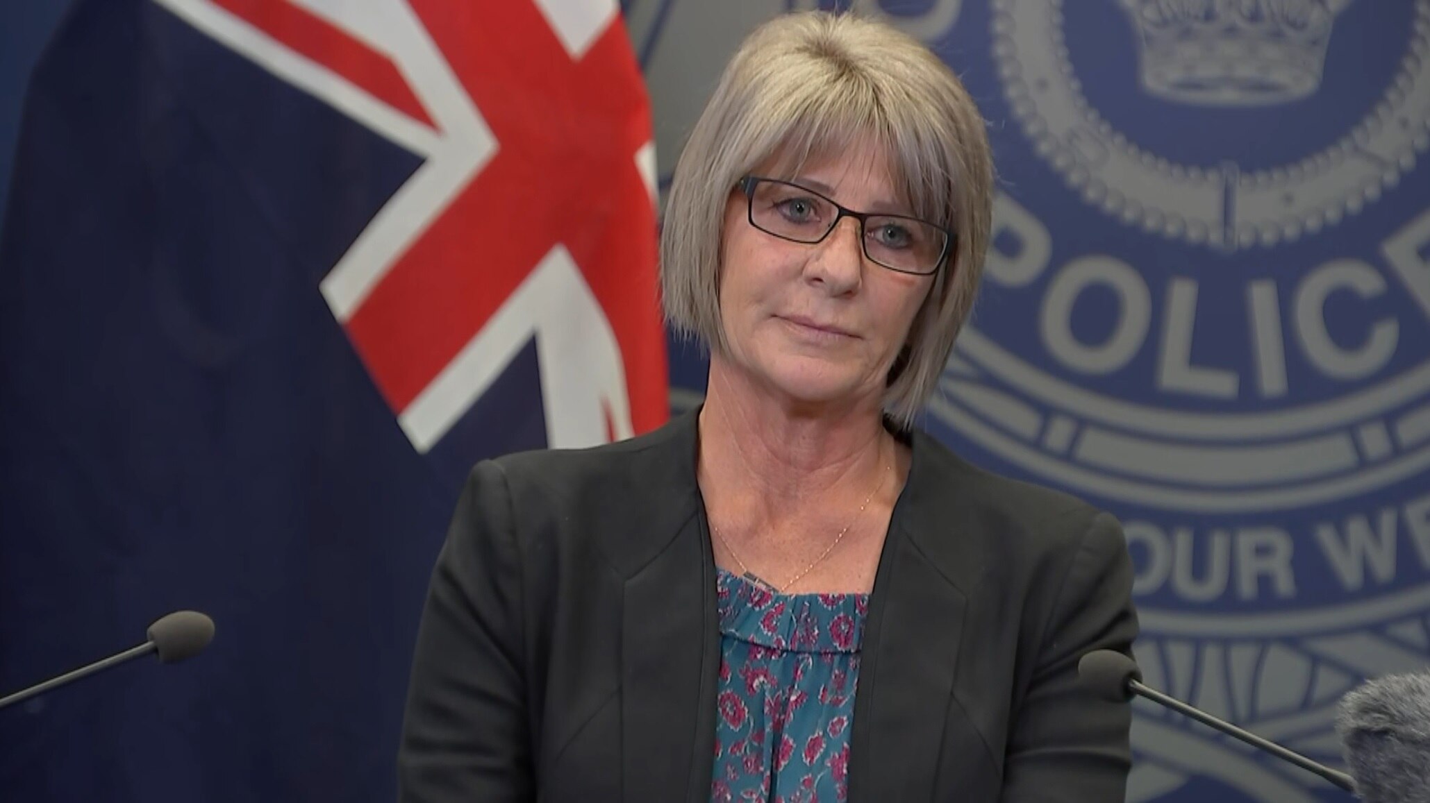 Kerry stands in front of microhpons, straight face, bob length hair, glasses.