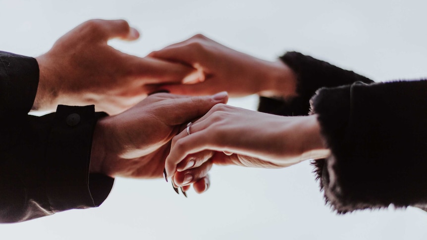 Close-up of man and woman holding hands in a story about how to support your partner without sacrificing yourself.